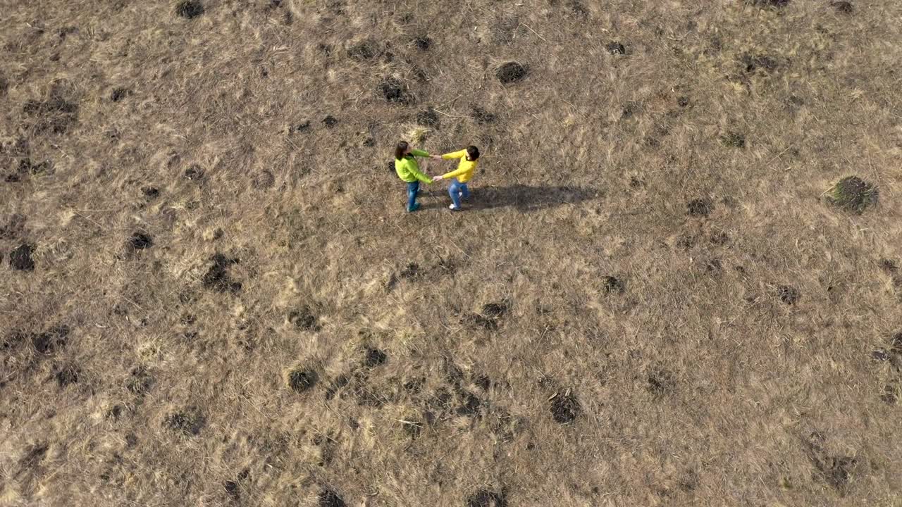 vista aérea de 4k de dos amigas tomadas de la mano, girando en un prado por un dron