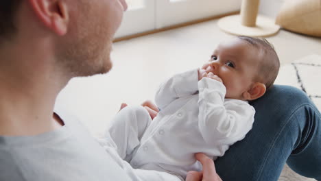 baby daughter lying on fathers lap as he plays game with her at home