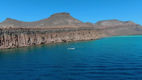 Aerial-view-Panning-shot,-a-tourist-boat-park-beside-the-Isla-Espiritu-Santo-in-Baja-Sur,-Mexico,-scenic-view-of-deep-blue-sea-and-mountain-range-in-the-background