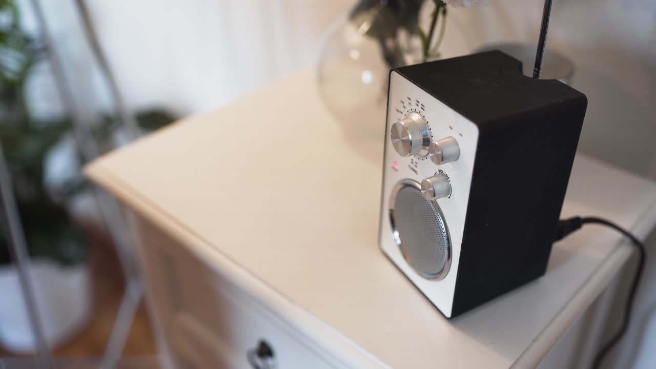 오래된 흰색 라디오를 켜는 노란색 스웨터를 입은 여성을 보여줍니다.