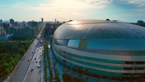 Aerial-view-of-traffic-on-road-in-Taipei-City-beside-modern-architecture-of-Dome-DaJudan-during-sunset