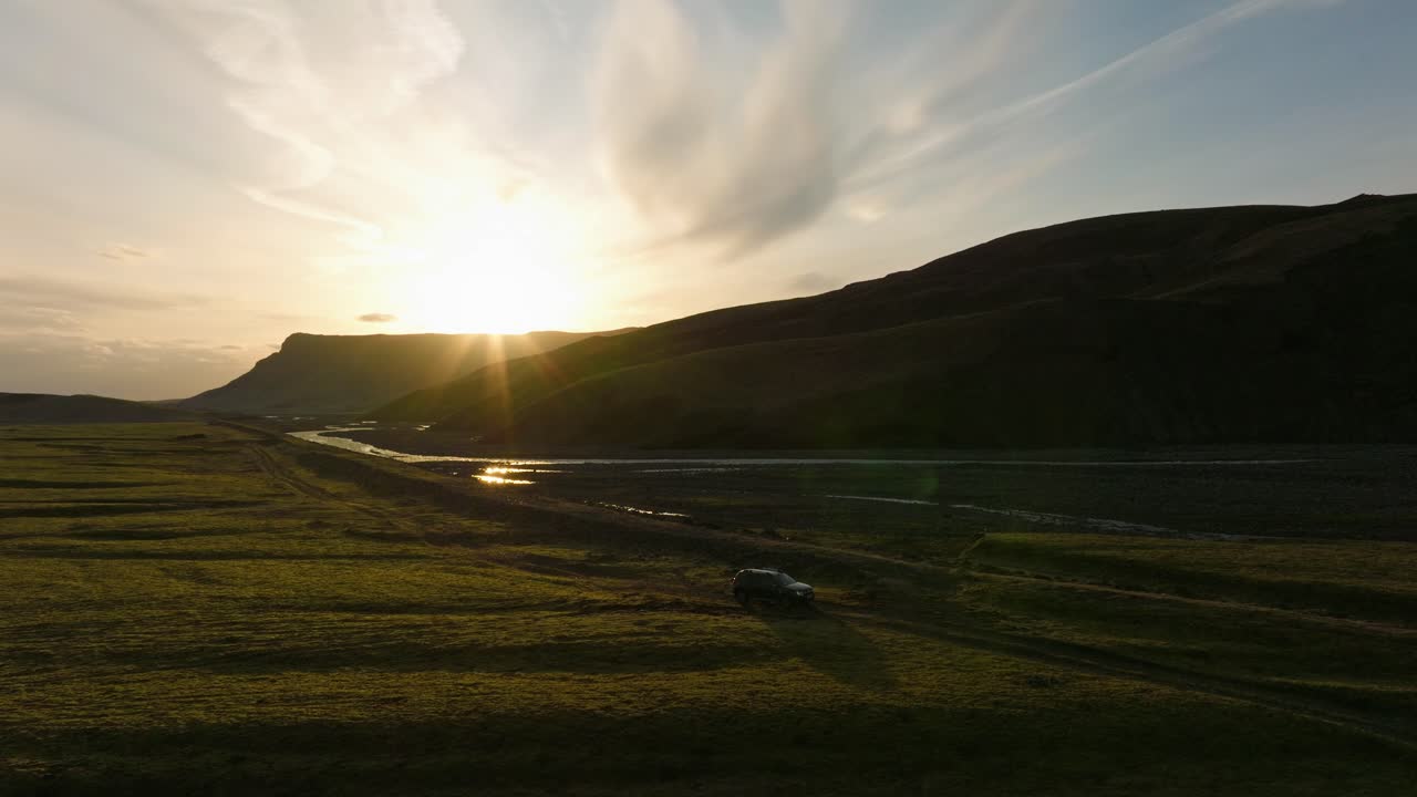 아이슬란드의 부르펠에 있는 계곡에 주차된 suv의 공중 사진, 멀리 떨어진 산 뒤에서 해가 지는 황금빛을 반사하는 강