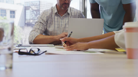 Diverse-male-and-female-business-colleagues-taking-notes-and-using-laptop-at-meeting