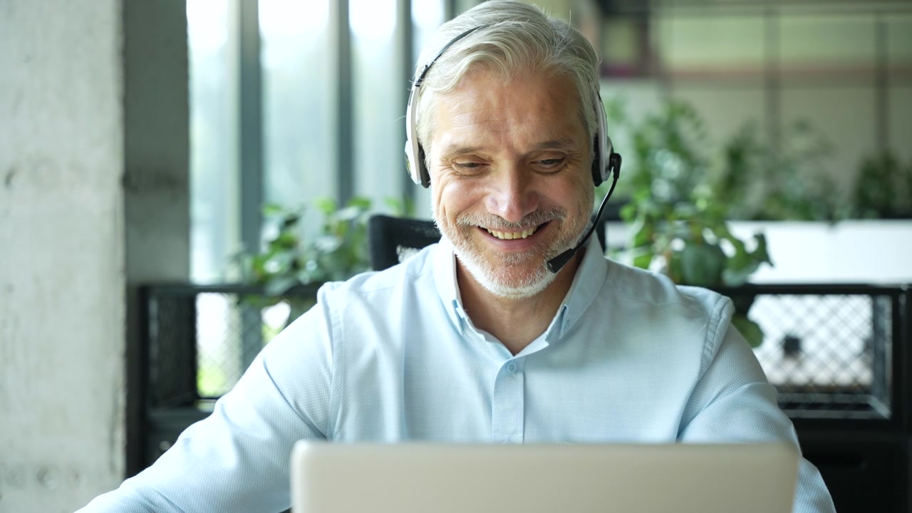 Uomo d'affari maturo con auricolare che fa una videochiamata sul laptop in ufficio.