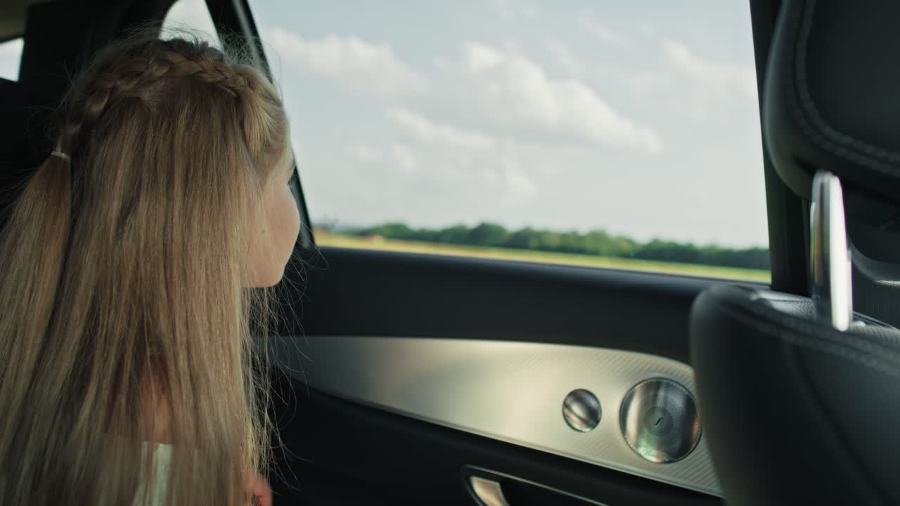 8살의 백인 소녀가 차 창문 밖을 보고 있습니다.