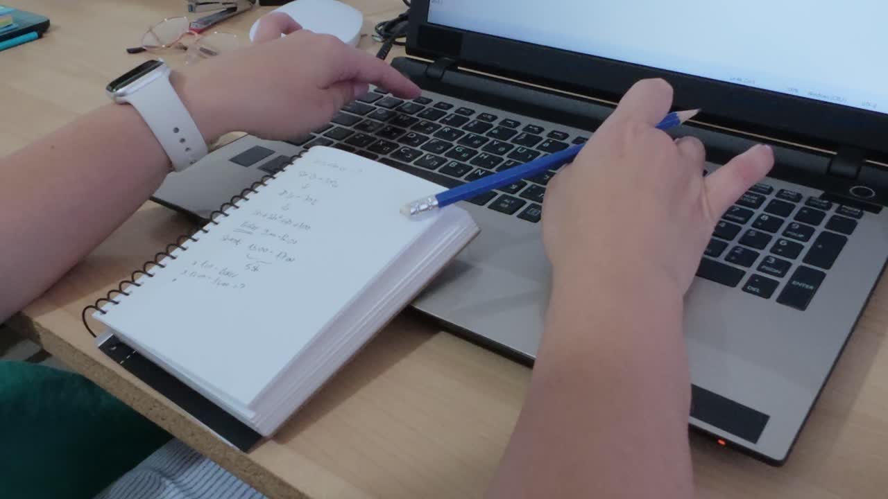 Detailed close-up of hands writing in notebook and typing on laptop keyboard.