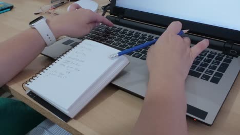 Detailed close-up of hands writing in notebook and typing on laptop keyboard.