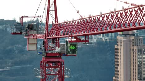 Tower-crane-operator-controlling-large-red-crane-constructing-skyscraper-in-downtown-American-city