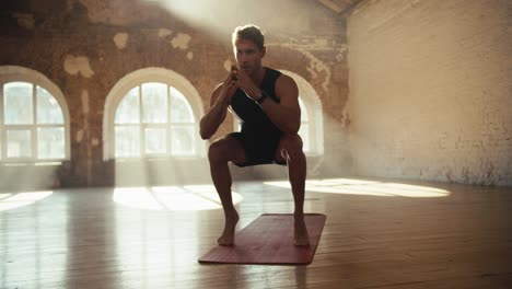 A-man-in-a-black-sports-uniform-does-exercises-and-squats-developing-calf-muscles-on-a-special-carpet-in-a-sunny-hall