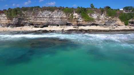 toma aérea en movimiento lateral de enormes acantilados en una playa en uluwatu, bali, indonesia, perspectiva interesante de la línea costera que muestra movimiento