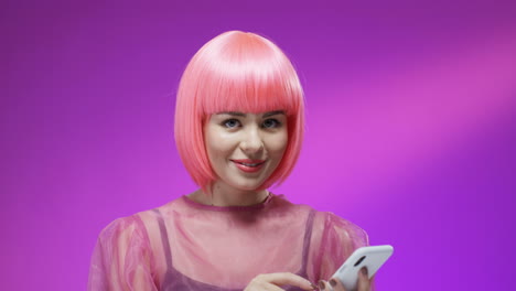 Close-Up-Of-Pretty-Woman-Wearing-A-Stylish-Pink-Wig-Smiling-Cheerfully-With-A-Smartphone-In-Her-Hands