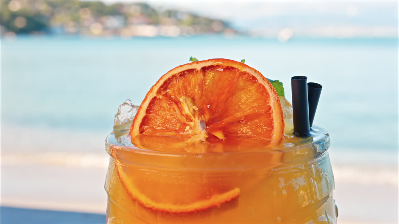 Primo piano di un cocktail arancione su un tavolo con una vista sfocata del mare sullo sfondo