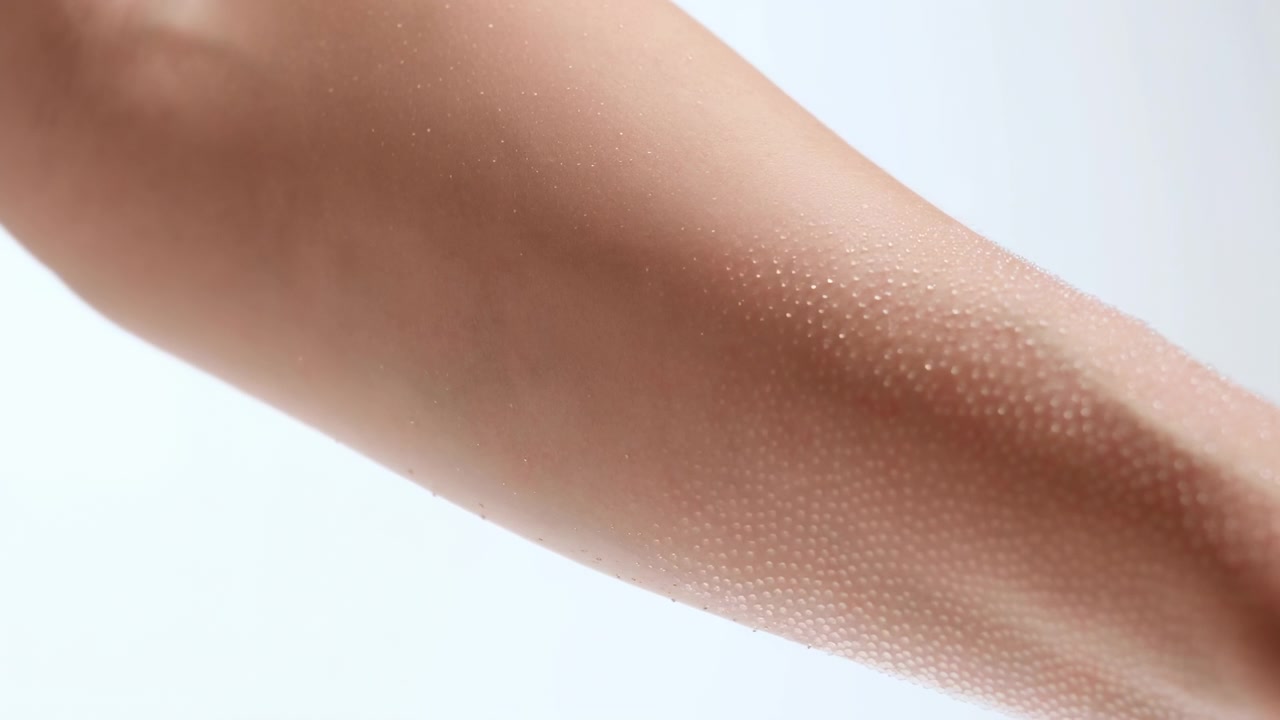 En bar menneskelig underarm strekker seg diagonalt over en lys hvit bakgrunn, som viser naturlig hudtekstur, myke skygger og en minimalistisk studiokomposisjon.