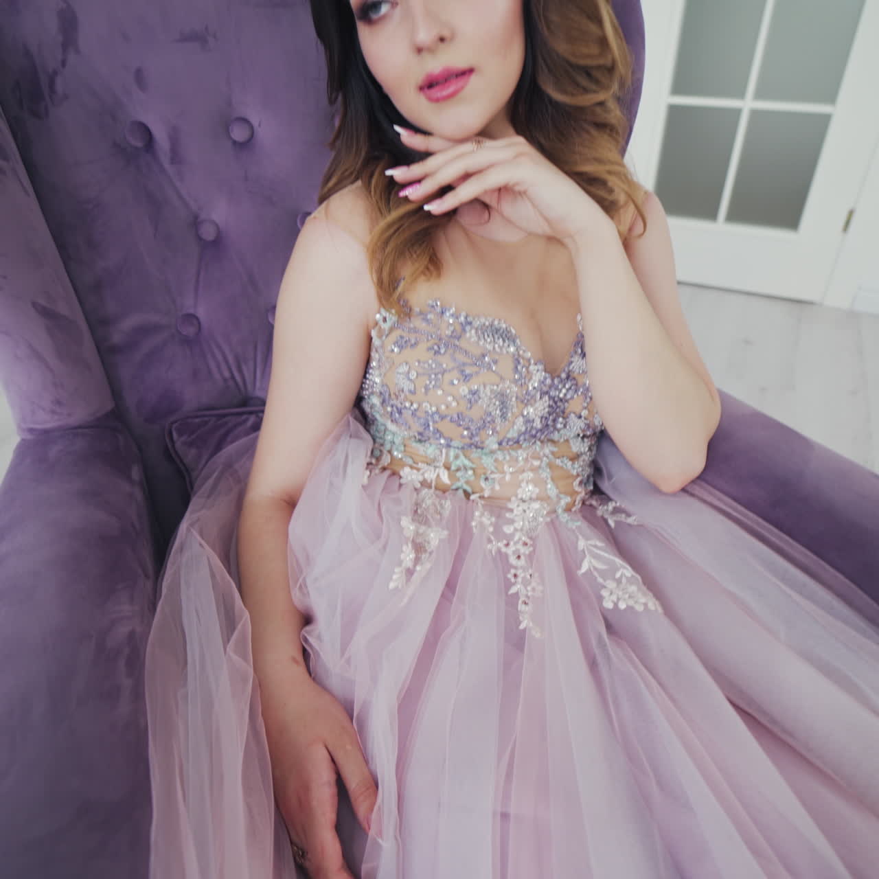Attractive girl in a sexy dress sitting in a purple armchair. Beauty gorgeous bride is posing in a nice interior room. Beautiful model in wedding dress. Camera moves up.