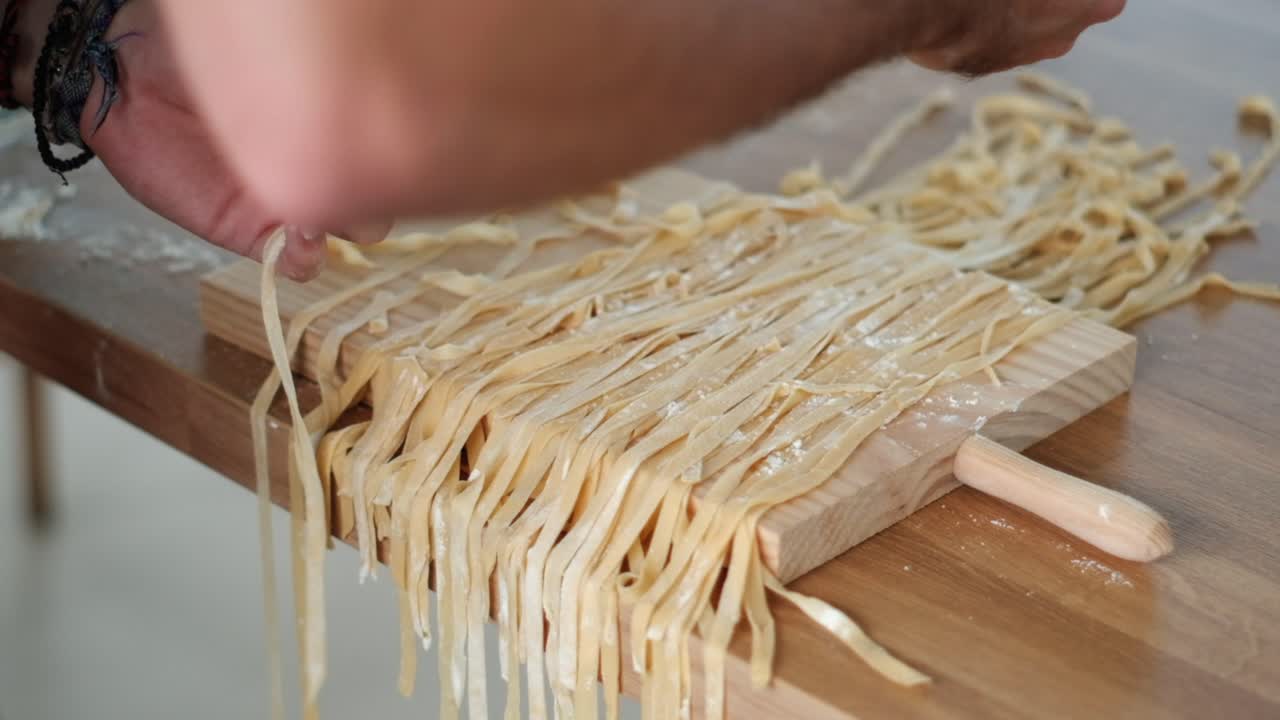 Primo piano cinematografico dello chef che previene l'adesione - Separazione delle tagliatelle con la farina