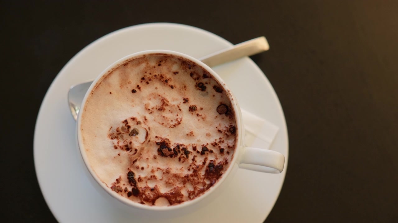 Cappuccino con schiuma cremosa e cacao in polvere in una tazza bianca, posizionato su un piattino con un cucchiaino. Bevanda rinfrescante per la mattina