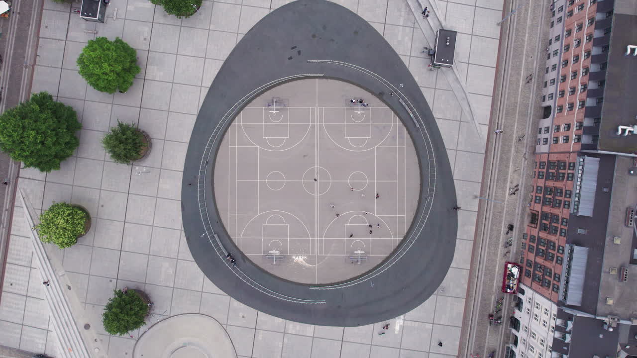 From a bird's-eye view, experience the liveliness of a basketball court at Israels Plads in Copenhagen during midday, with its dynamic urban setting and bustling crowds