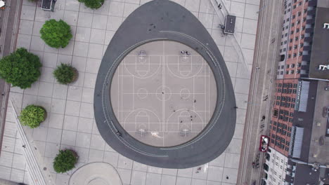 From a bird&#039;s-eye view, experience the liveliness of a basketball court at Israels Plads in Copenhagen during midday, with its dynamic urban setting and bustling crowds