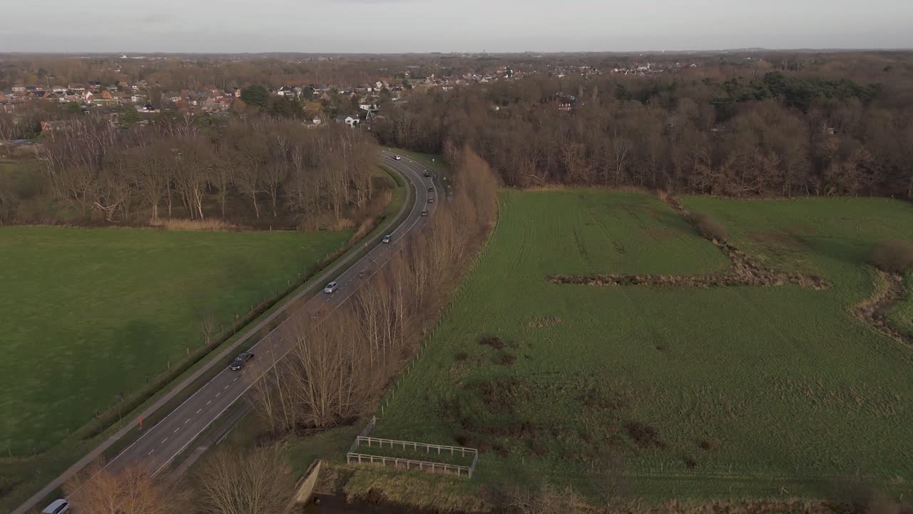 Drone shot of cars on a road passing through grass lands and nature on a province road during a sunny day.
