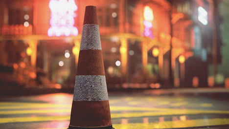 traffic cone placed on a wet street under neon lights at night