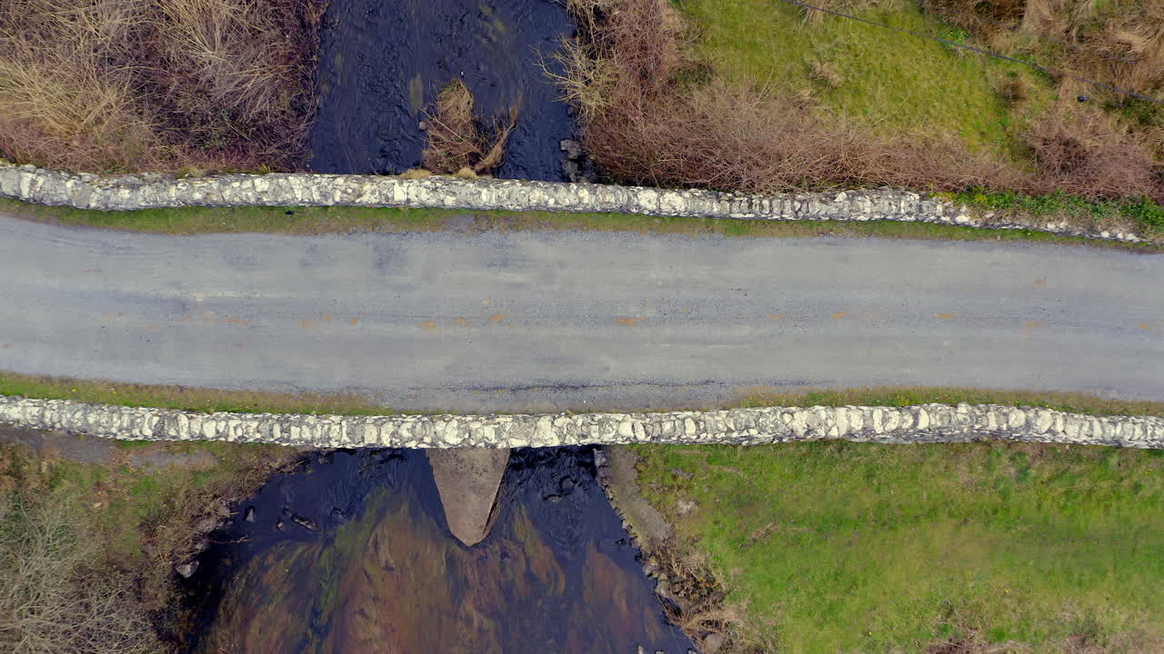 Top-down aerial ascends from pavement to wide view of Quiet Man Bridge and river