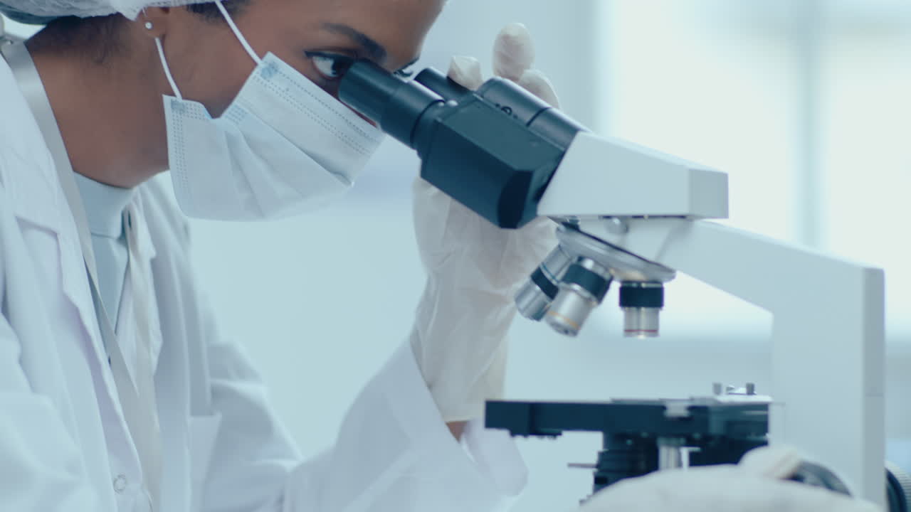 保護用医用ユニフォームを着た女性研究員が微鏡を使っています