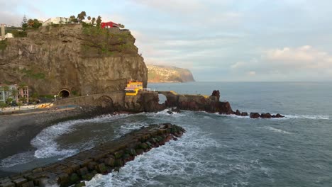 Drohne-Umkreist-Wellenbrecher-Und-Strand-Der-Küstenstadt-Ponta-Do-Sol-Auf-Madeira,-Portugal