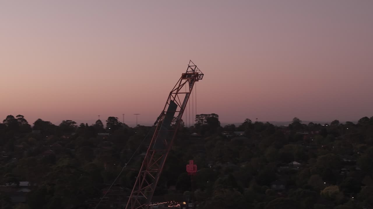 Drone video capturing a rotating crane silhouette against a dusky Melbourne skyline in Ringwood. The serene twilight ambiance highlights urban construction progress