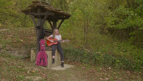 Singer-songwriter-female-guitarist-rehearses-by-forest-wishing-well