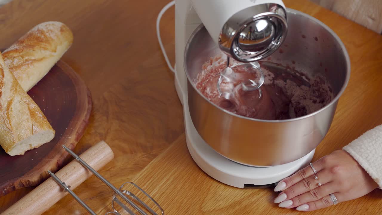 Women hands rotating bowl as counter mixer whisks the batter