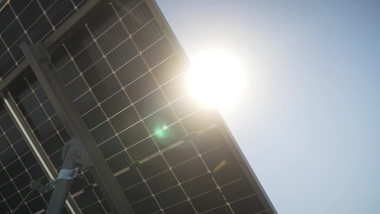 Ripresa dal basso di pannelli solari, che enfatizza il design fotovoltaico e l'efficienza nell'uso di energia pulita, panoramica a destra mentre un bagliore solare fiorisce e risplende