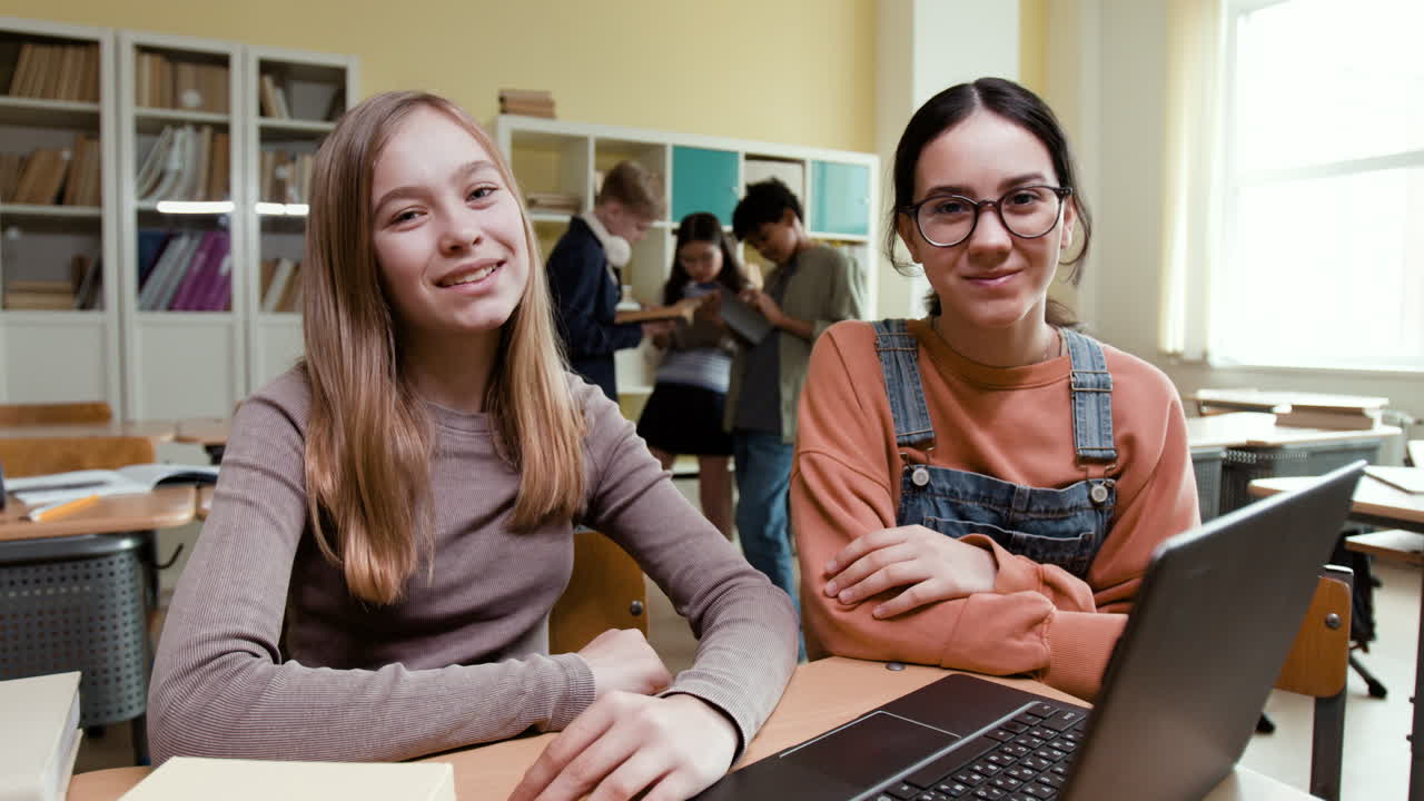 Two smiling students in a classroom with a laptop