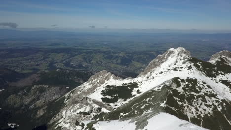 Snowy-Polish-mountain-aerial-looks-past-summit-down-into-Slovakia