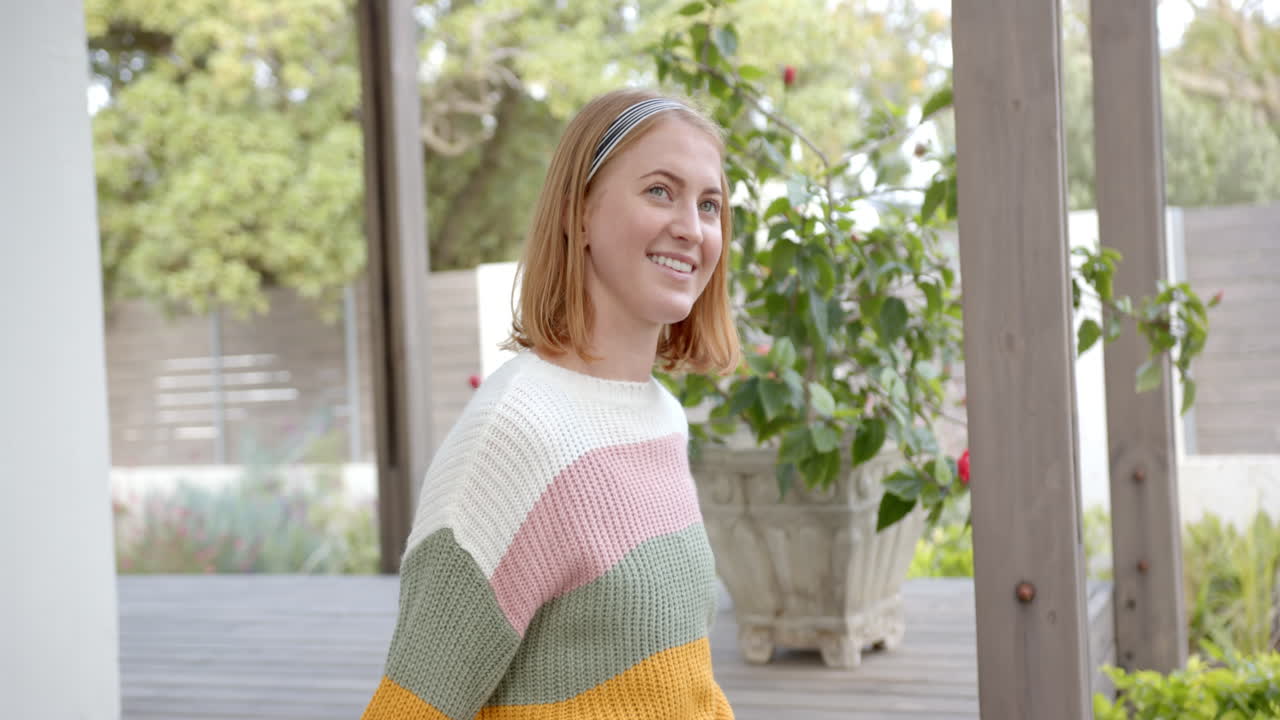 Lächelnde Frau in farbenfrohem Pullover steht auf der Veranda und genießt den Ausblick.