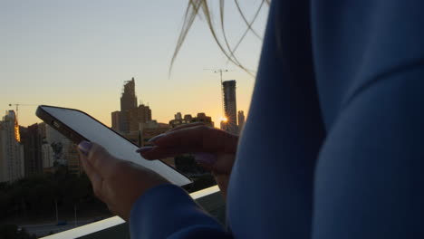 mujer enviando mensajes de texto en el móvil contra el paisaje urbano de la mañana con el sol naciente