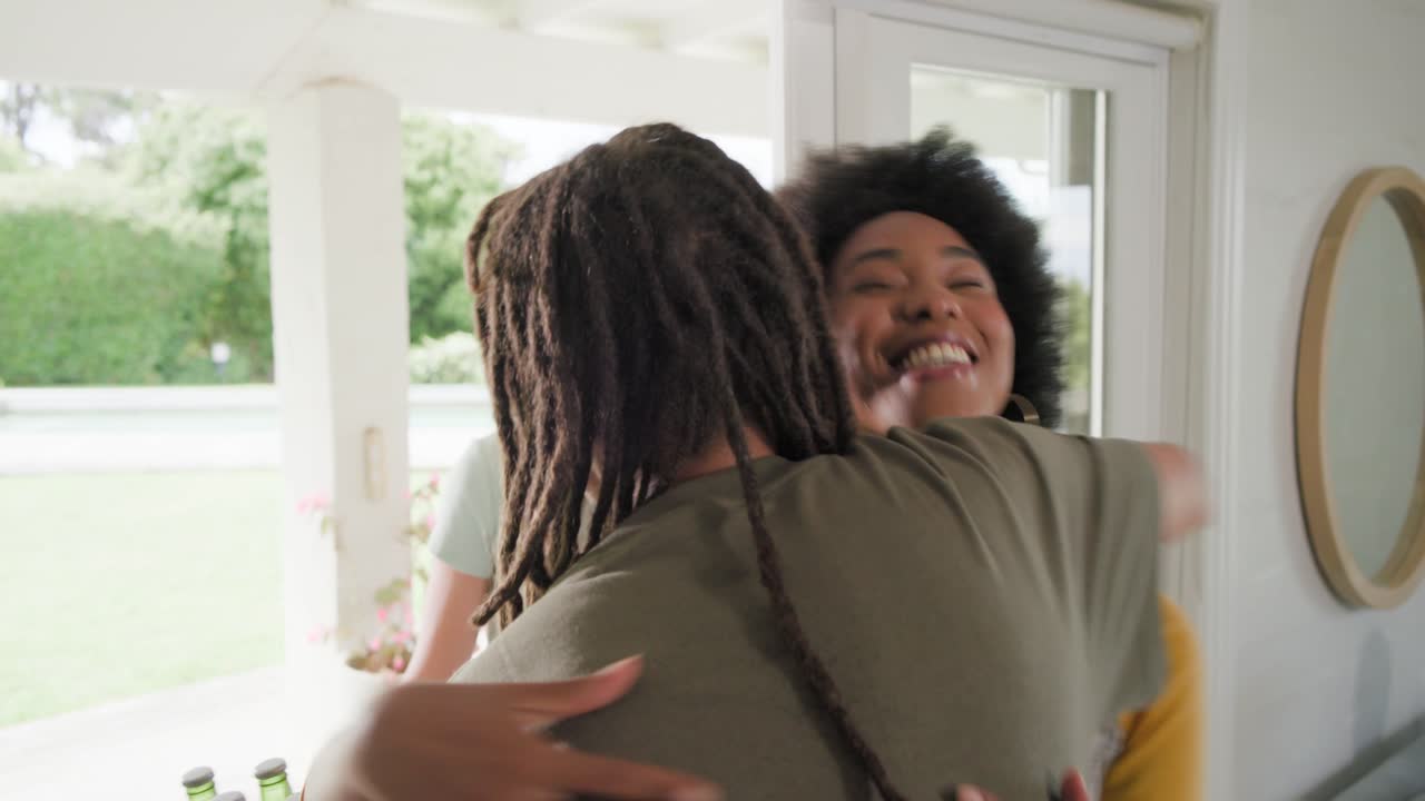 Diverse friends arriving at sliding door, man with dreads taking sixpack and carrying rose to visit