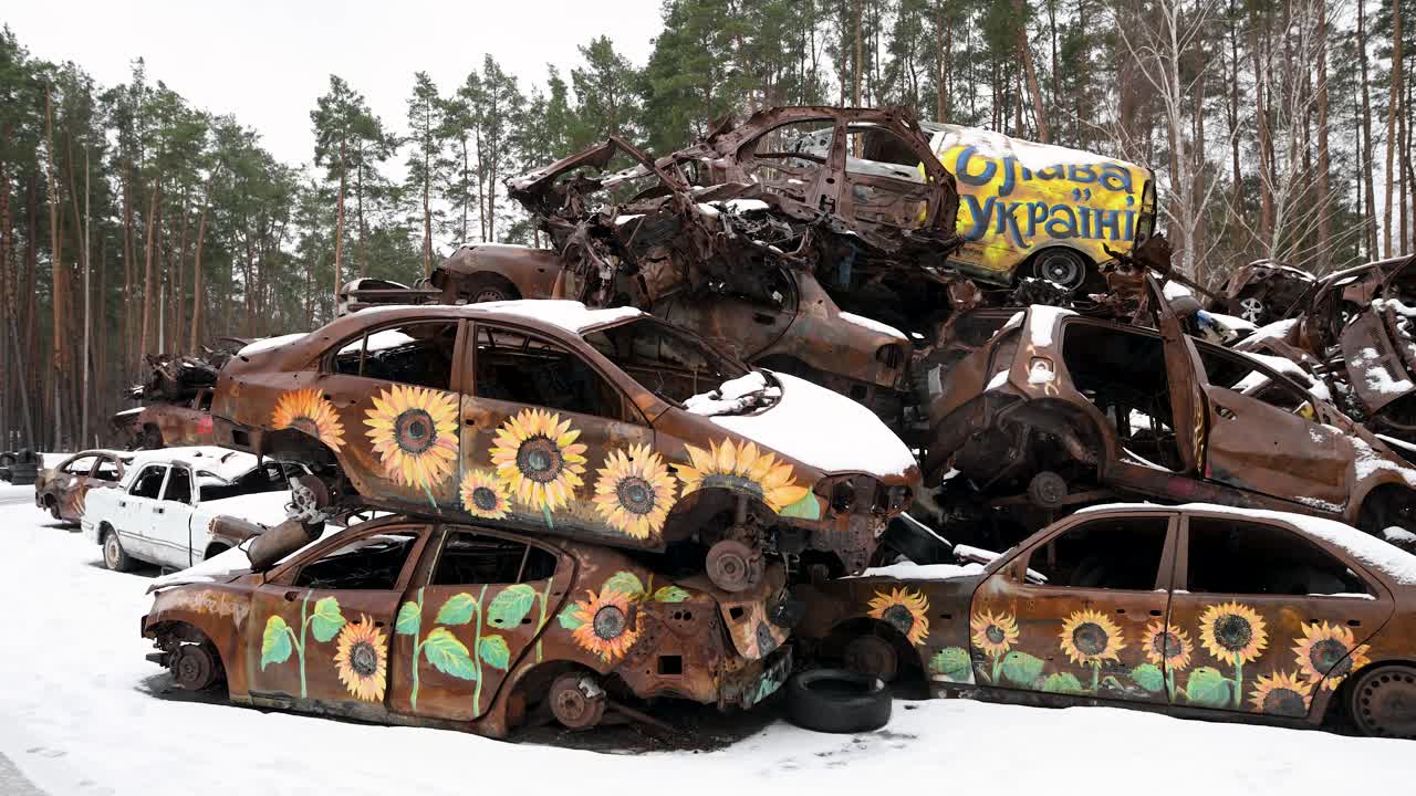 On a winter day in Irpin, Ukraine, a pile of burnt and destroyed cars is stacked, with some vehicles painted with sunflower drawings, after intense battles between Ukrainian and Russian forces.