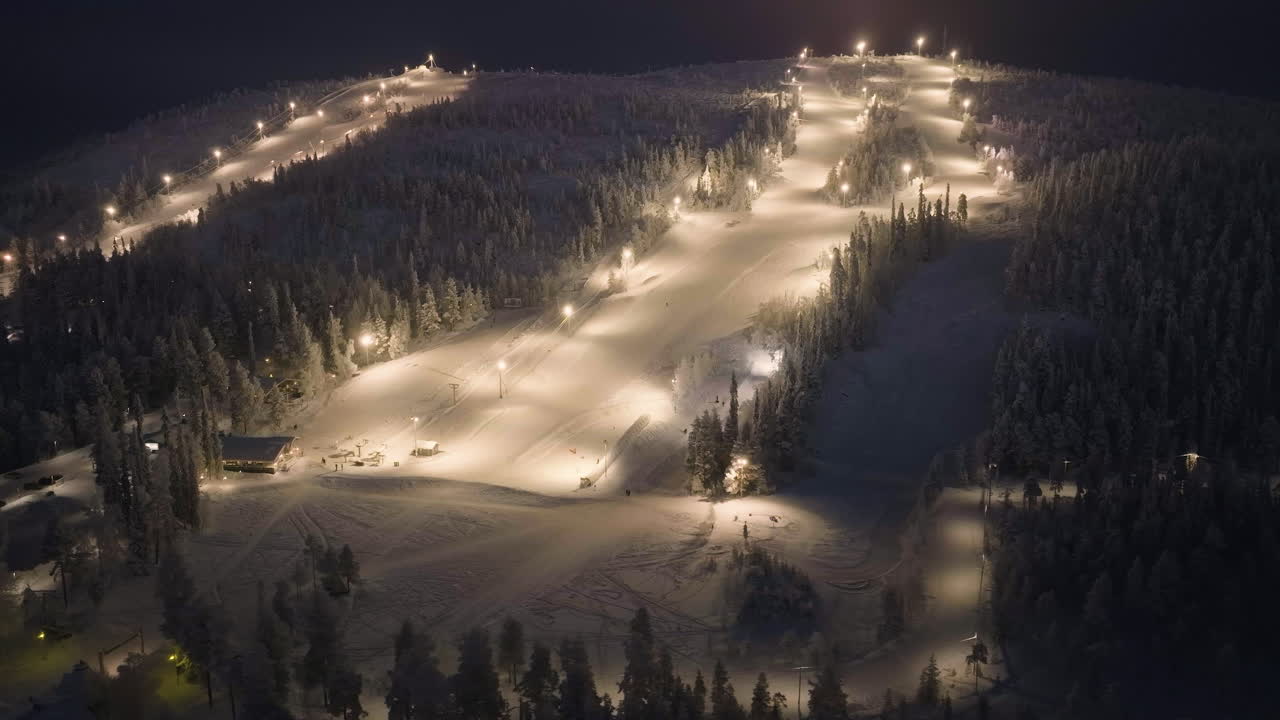 Aerial view circling the illuminated slopes of Salla, winter evening in Finland