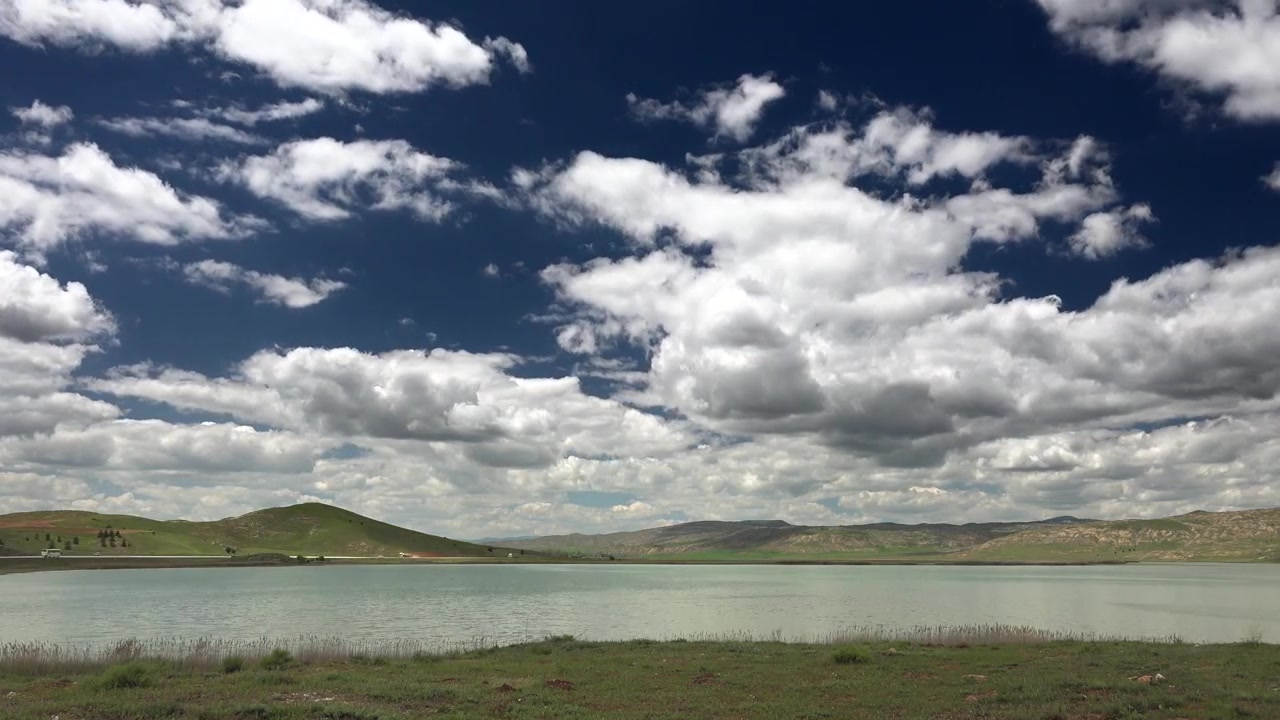 Vista panoramica di un lago calmo con colline ondulate e cielo nuvoloso