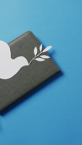 vertical video of white dove with leaf on grey notebook and copy space on blue background