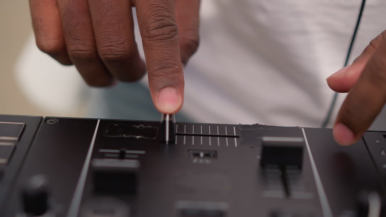 closeup black DJ fingers on fader, street busker mixing on portable controller, outdoor practice session, casual denim attire, headphones around neck, sunlight highlights, urban corner vibe, tutor