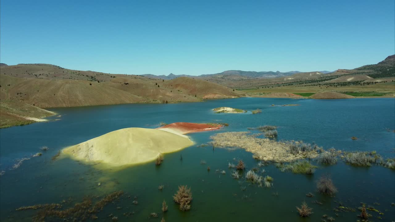 US, Oregon, Prineville, Painted Hills, 2025-05-05 - Drone view over the lake at Painted Hills in the John Day Fossil Beds National Monument, red mountain, green fields, and hills in central Oregon