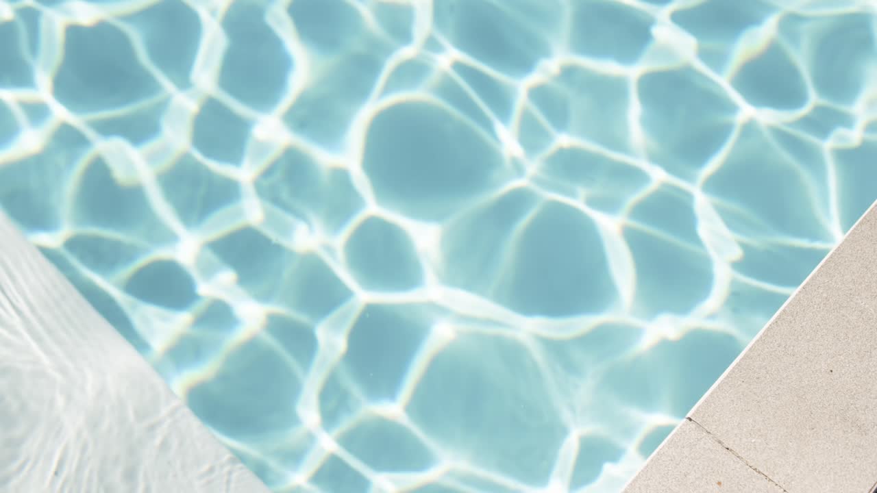 Sudut kolam renang menunjukkan air biru pucat berkilauan dengan kaustik cerah dan bantal putih mengambang.