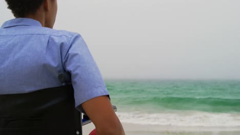 vista trasera de un hombre afroamericano sentado en silla de ruedas en la playa 4k