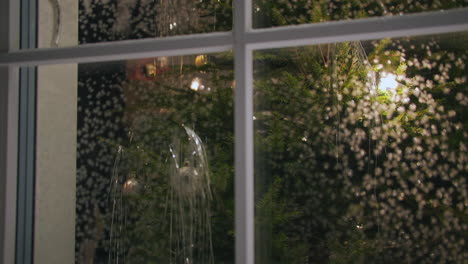 mujer decora un árbol de navidad en un hogar cálido y acogedor, filmado desde el exterior a través de una ventana helada