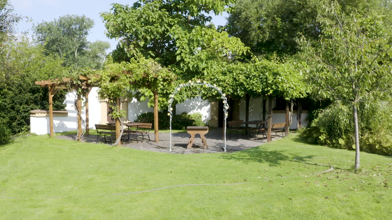 Arco nuziale decorato in un pittoresco giardino con posti a sedere, prato e alberi.