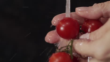manos enjuagando suavemente los tomates cherry rojos maduros uno por uno bajo el grifo de agua - toma de primer plano