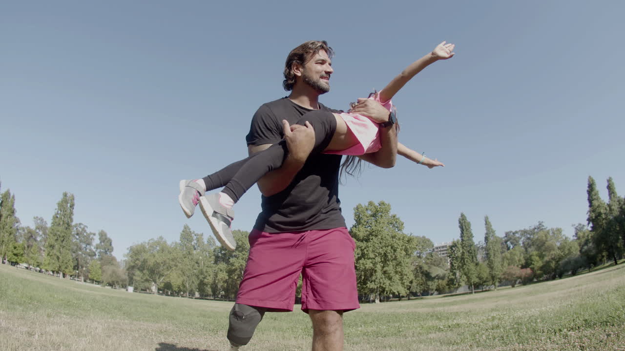 padre feliz con pierna protésica dando vueltas a su hija en las manos