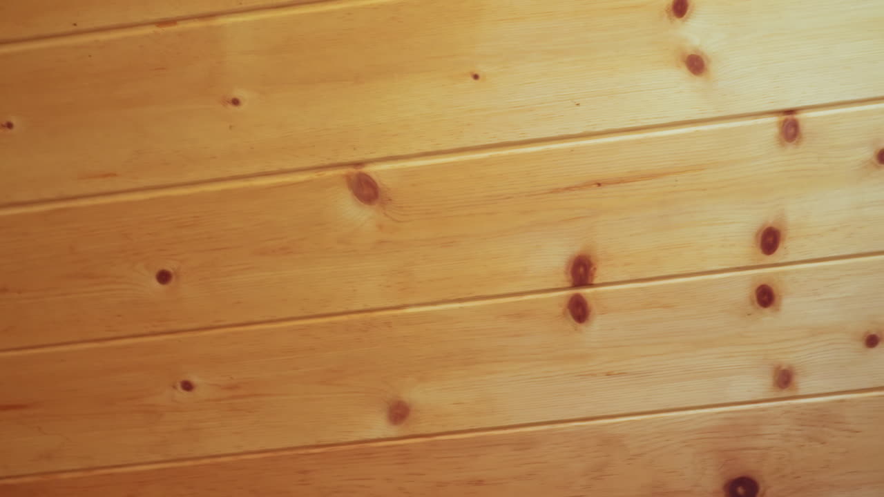 Close up of wooden room showing vertical wall paneling meeting ceiling corner, featuring light honey toned wood grain, natural knots, and soft lighting that emphasize calm