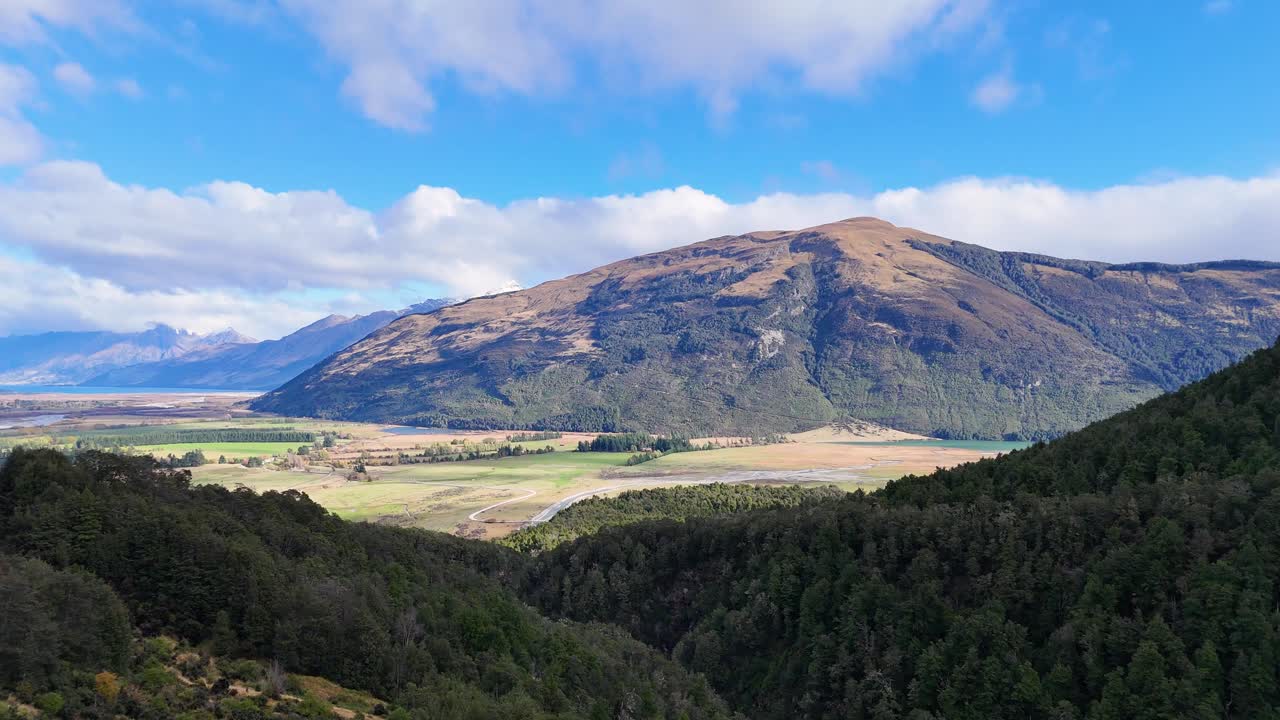 Panoramic view of Glenorchy's mountains under clear skies, showcasing lush greenery and expansive landscapes with natural lighting